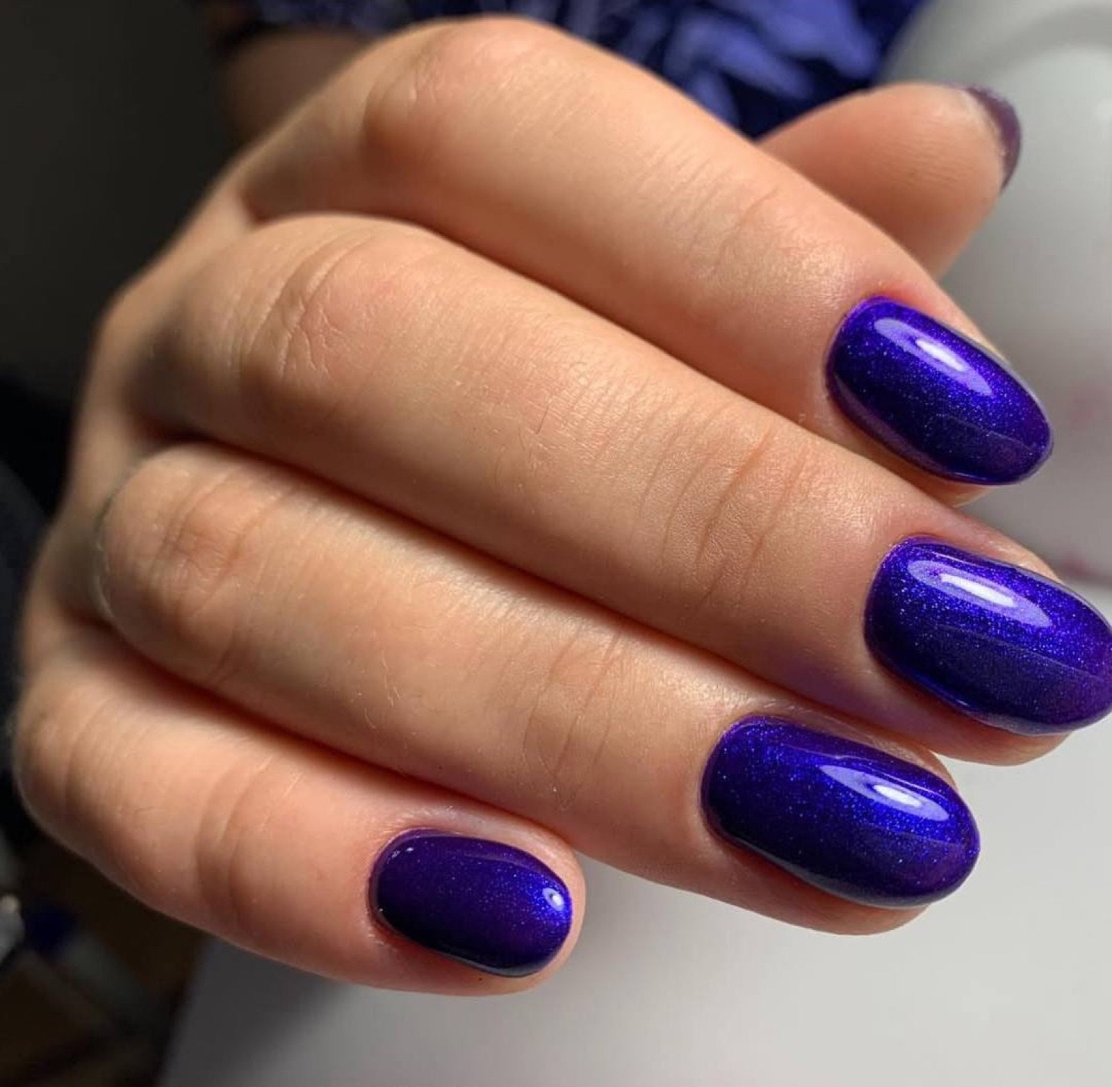 Nail design inspiration for builder gel nails near me: Close-up of a hand with glossy purple glitter nail polish showing four fingernails in an oval shape