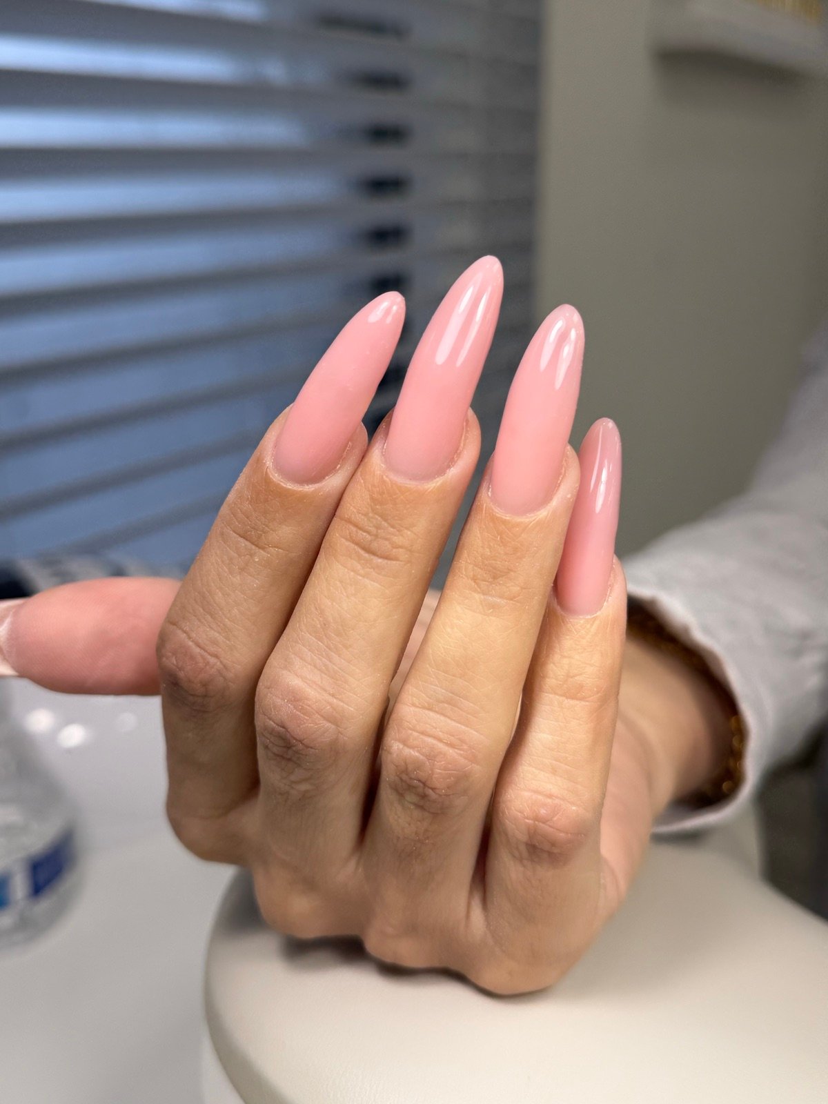 Nail design inspiration for builder gel nails near me: Close-up of a hand with long almond-shaped nails in glossy pink finish, showing natural skin texture and professional