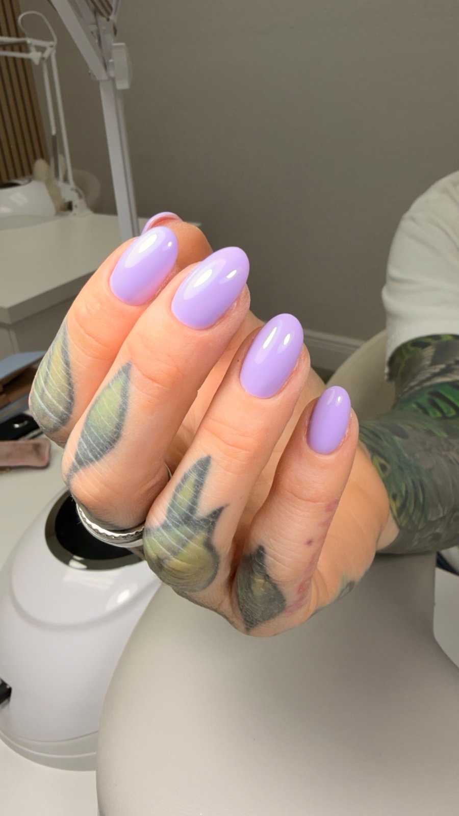 Nail design inspiration for builder gel Tampa: Close-up of a hand with glossy lavender manicure and finger tattoos in a nail studio setting