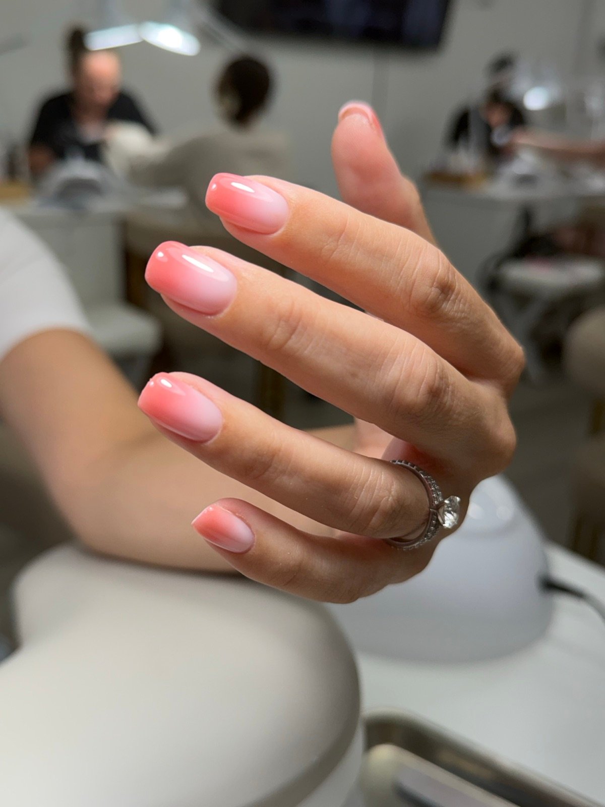 Nail design inspiration for dry manicure Tampa: Close-up of a hand with soft pink ombre manicured nails, glossy finish, oval shape, medium length, wearing a ring on the finger