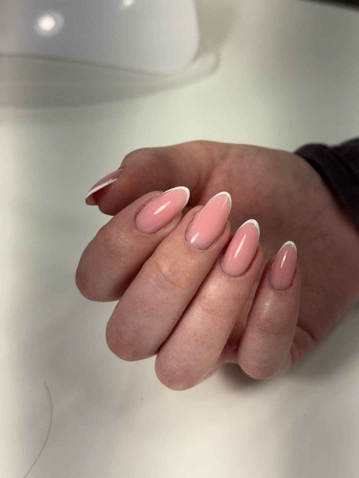 Nail design inspiration for russian manicure near me: Close-up of a hand with soft pink gradient nails featuring white French tips, glossy finish, and natural nail beds.