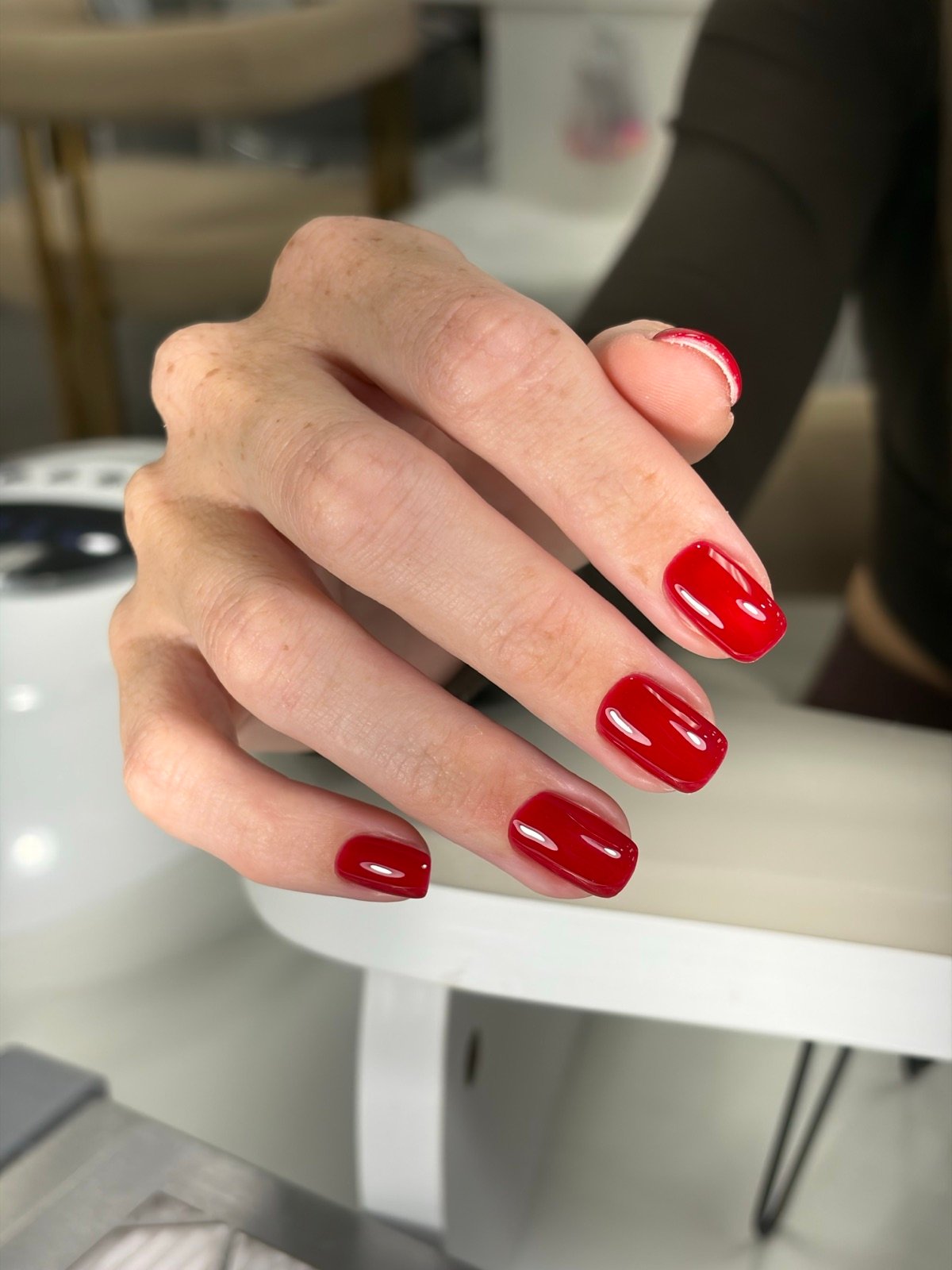 Nail design inspiration for russian manicure near me: Close-up of a hand with glossy red square-shaped nails in a salon setting