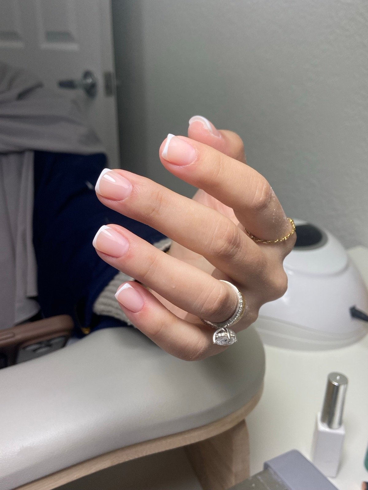 Nail design inspiration for russian nail salon: Close-up of a hand with French tip manicure showing nude pink nails with white tips, glossy finish, and rings on fingers in a salon