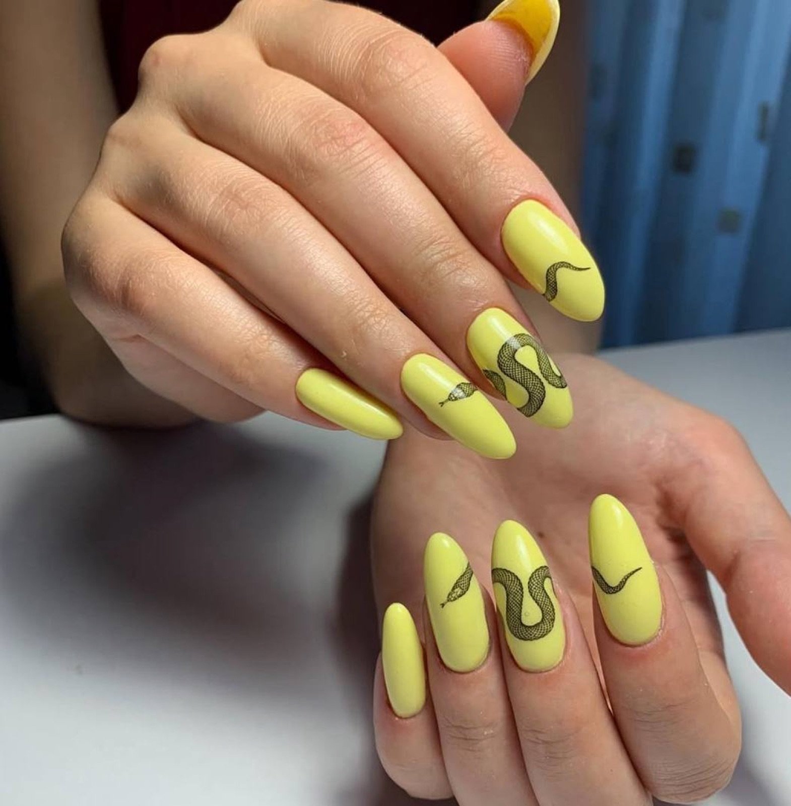 Nail design inspiration for russian nail salon: Close-up of hands with yellow manicure featuring black snake nail art, glossy finish, almond-shaped long nails