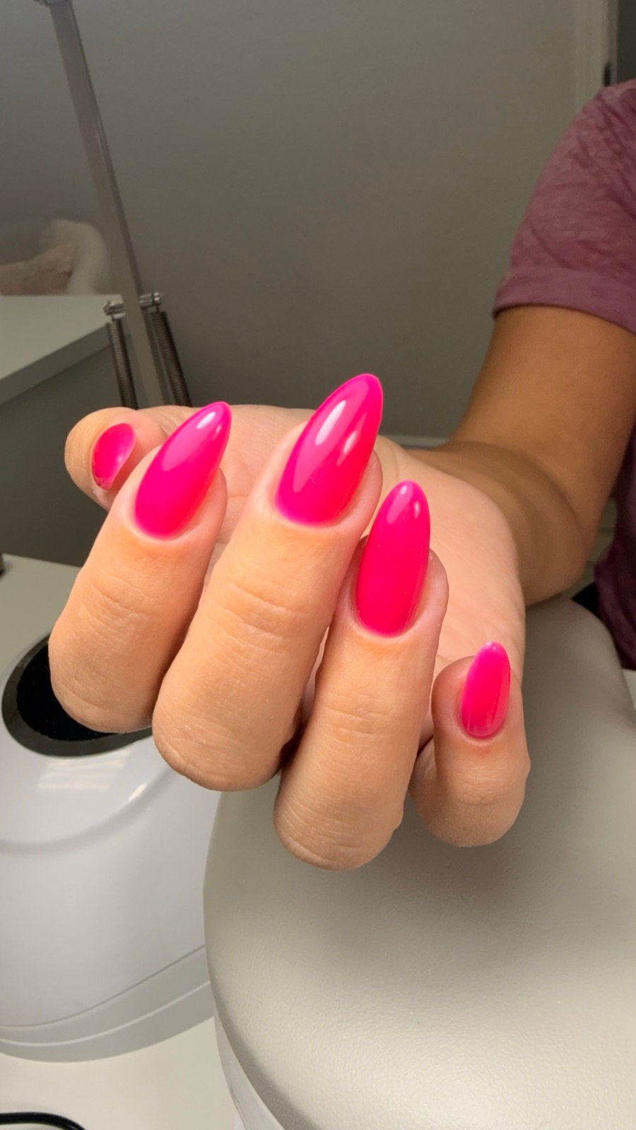 Nail design inspiration for russian nails near me: Close-up of a hand with bright pink stiletto-shaped long nails featuring glossy finish in a nail salon setting